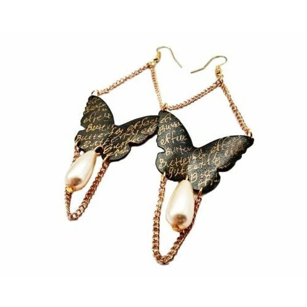 Τα εντυπωσιακά χειρόγραφα σκουλαρίκια πεταλούδα με αλυσίδα και πέρλες αποτελούν ένα μοναδικό statement κόσμημα που συνδυάζει τη θηλυκότητα με τη σύγχρονη αισθητική. Σχεδιασμένα από την Ελληνίδα Σχεδιάστρια Κοσμημάτων Αικατερίνη Χαλκιαδάκη, αυτά τα χειροποίητα σκουλαρίκια φέρουν χειρόγραφα στοιχεία που προσδίδουν μια ποιητική διάσταση στο design.\u000AΗ μαύρη πατίνα στον ορείχαλκο δημιουργεί έναν vintage χαρακτήρα, ενώ οι λεπτές χρυσαφί αλυσίδες και οι κλασικές πέρλες προσθέτουν κομψότητα και κίνηση. Η πεταλούδα, σύμβολο μεταμόρφωσης και ελευθερίας, γίνεται το κεντρικό στοιχείο αυτών των κρεμαστών σκουλαρικιών, ιδανικών για ιδιαίτερες εμφανίσεις και γαμήλιες εκδηλώσεις.