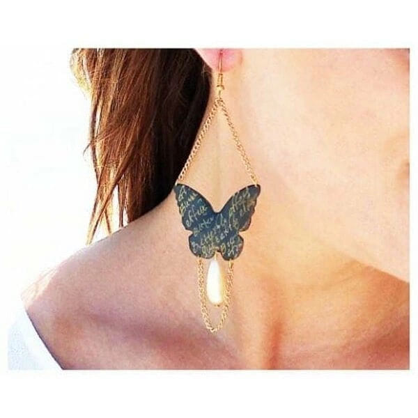 Χειρόγραφα μεγάλα σκουλαρίκια πεταλούδες με αλυσίδα και πέρλες - 3019, Τα εντυπωσιακά χειρόγραφα σκουλαρίκια πεταλούδα με αλυσίδα και πέρλες αποτελούν ένα μοναδικό statement κόσμημα που συνδυάζει τη θηλυκότητα με τη σύγχρονη αισθητική. Σχεδιασμένα από την Ελληνίδα Σχεδιάστρια Κοσμημάτων Αικατερίνη Χαλκιαδάκη, αυτά τα χειροποίητα σκουλαρίκια φέρουν χειρόγραφα στοιχεία που προσδίδουν μια ποιητική διάσταση στο design.
Η μαύρη πατίνα στον ορείχαλκο δημιουργεί έναν vintage χαρακτήρα, ενώ οι λεπτές χρυσαφί αλυσίδες και οι κλασικές πέρλες προσθέτουν κομψότητα και κίνηση. Η πεταλούδα, σύμβολο μεταμόρφωσης και ελευθερίας, γίνεται το κεντρικό στοιχείο αυτών των κρεμαστών σκουλαρικιών, ιδανικών για ιδιαίτερες εμφανίσεις και γαμήλιες εκδηλώσεις.