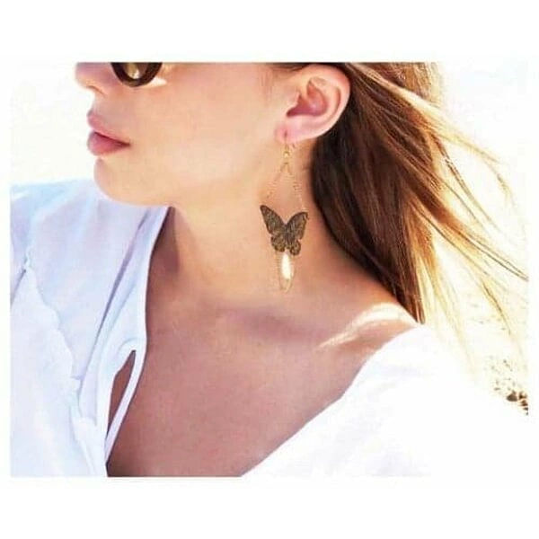 Χειρόγραφα μεγάλα σκουλαρίκια πεταλούδες με αλυσίδα και πέρλες - 3019, Τα εντυπωσιακά χειρόγραφα σκουλαρίκια πεταλούδα με αλυσίδα και πέρλες αποτελούν ένα μοναδικό statement κόσμημα που συνδυάζει τη θηλυκότητα με τη σύγχρονη αισθητική. Σχεδιασμένα από την Ελληνίδα Σχεδιάστρια Κοσμημάτων Αικατερίνη Χαλκιαδάκη, αυτά τα χειροποίητα σκουλαρίκια φέρουν χειρόγραφα στοιχεία που προσδίδουν μια ποιητική διάσταση στο design.
Η μαύρη πατίνα στον ορείχαλκο δημιουργεί έναν vintage χαρακτήρα, ενώ οι λεπτές χρυσαφί αλυσίδες και οι κλασικές πέρλες προσθέτουν κομψότητα και κίνηση. Η πεταλούδα, σύμβολο μεταμόρφωσης και ελευθερίας, γίνεται το κεντρικό στοιχείο αυτών των κρεμαστών σκουλαρικιών, ιδανικών για ιδιαίτερες εμφανίσεις και γαμήλιες εκδηλώσεις.