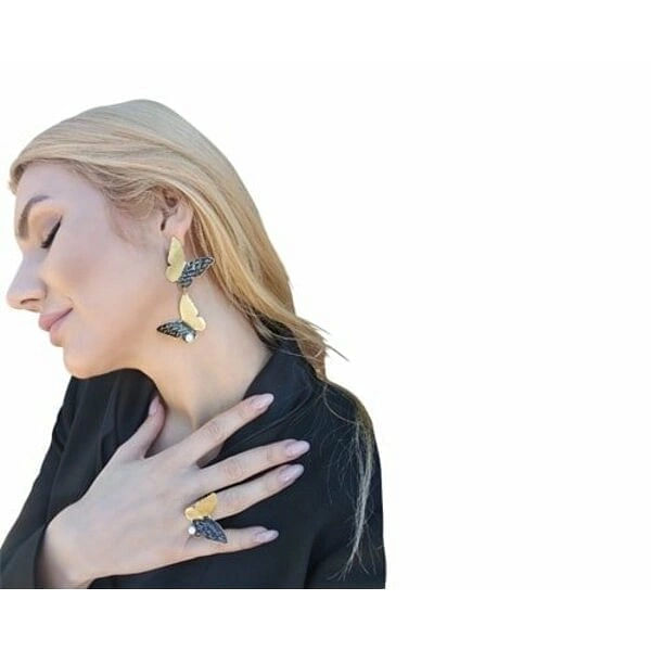 Μεγάλα εντυπωσιακά σκουλαρίκια πεταλούδα με μαργαριτάρια - 4645, Τα εντυπωσιακά σκουλαρίκια πεταλούδα με μαργαριτάρια αποτελούν ένα μοναδικό κόσμημα που συνδυάζει τη φυσική ομορφιά με την καλλιτεχνική δημιουργία. Σχεδιασμένα από την Ελληνίδα Σχεδιάστρια Κοσμημάτων Αικατερίνη Χαλκιαδάκη, αυτά τα χειροποίητα σκουλαρίκια αποτυπώνουν την κομψότητα της πεταλούδας σε έναν πρωτότυπο σχεδιασμό που αιχμαλωτίζει το βλέμμα.
Κατασκευασμένα από υψηλής ποιότητας ορείχαλκο με μαύρη πατίνα, τα σκουλαρίκια διαθέτουν διπλό σχήμα πεταλούδας που δημιουργεί μια εκπληκτική οπτική ισορροπία. Τα φυσικά μαργαριτάρια προσθέτουν μια τελειοποιητική πινελιά λάμψης, ενώ οι χρυσαφί αποχρώσεις δίνουν ζεστασιά στο σύνολο. Το κρεμαστό σχήμα και το μεγάλο μέγεθος τα καθιστούν ιδανικά για γάμους, βραδινές εξόδους ή ειδικές περιστάσεις.
