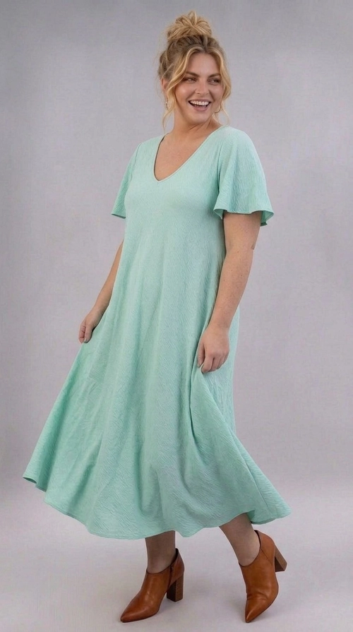 Φόρεμα πράσινο καλοκαιρινό - FRW806 | Candiashop Boutique, Ένα υπέροχο maxi φόρεμα σε παστέλ χρώμα μέντας που θα σας κάνει να ξεχωρίσετε σε κάθε περίσταση. Το μονόχρωμο σχέδιό του με ελαφρώς υφασμένη υφή προσδίδει μια εκλεπτυσμένη αίσθηση πολυτέλειας, ενώ η γραμμή Α που ακολουθεί δημιουργεί μια ρέουσα σιλουέτα που κολακεύει κάθε σώμα. Η V-λαιμόκοψη πλαισιώνει αρμονικά το ντεκολτέ, ενώ τα φαρδιά βολάν μανίκια προσθέτουν μια ρομαντική, θηλυκή πινελιά στο σύνολο. Ιδανικό για plus size γυναίκες που αναζητούν άνεση χωρίς να θυσιάζουν το στυλ. Το φόρεμα αυτό είναι τέλειο για καλοκαιρινές εκδρομές, γαμήλιες δεξιώσεις, βαπτίσεις ή ρομαντικά δείπνα. Μπορεί να συνδυαστεί με καφέ δερμάτινα πέδιλα με τακούνι, όπως στη φωτογραφία, για ένα ολοκληρωμένο, κομψό αποτέλεσμα, ή εναλλακτικά με λευκά sneakers για ένα πιο casual look. Η ελαφριά υφή του υφάσματος το καθιστά ιδανικό για τις ζεστές καλοκαιρινές μέρες, προσφέροντας άνεση και στυλ ταυτόχρονα.