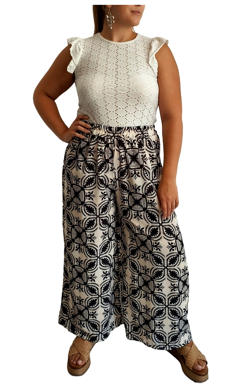 Κομψή και άνετη, αυτή η γυναικεία παντελόνα συνδυάζει αρμονικά την κομψότητα με την καθημερινή πρακτικότητα. Το επάνω μέρος του συνόλου αποτελείται από μια εκρού μπλούζα με διάτρητο κεντητό σχέδιο και χαριτωμένα βολάν στα μανίκια, προσδίδοντας μια θηλυκή και ρομαντική πινελιά. Η φαρδιά παντελόνα σε απαλό μπεζ φόντο με έντονο μαύρο γεωμετρικό μοτίβο δημιουργεί αντίθεση και προσφέρει εξαιρετική άνεση κατά την κίνηση. Η ψηλή μέση με το κορδόνι αναδεικνύει τη σιλουέτα, ενώ το φαρδύ πόδι χαρίζει αέρινη αίσθηση ιδανική για τις ζεστές καλοκαιρινές ημέρες. Φορέστε αυτό το σύνολο με πλατφόρμες ή επίπεδα σανδάλια για καθημερινές βόλτες, ή συνδυάστε το με κοσμήματα και ψηλά πέδιλα για απογευματινές εξόδους. Το υφασμάτινο υλικό είναι ελαφρύ και διαπνέον, κατάλληλο για άνετες εμφανίσεις από το πρωί ως το βράδυ, ενώ η ευκολία στο συνδυασμό το καθιστά απαραίτητο κομμάτι για κάθε καλοκαιρινή γκαρνταρόμπα.