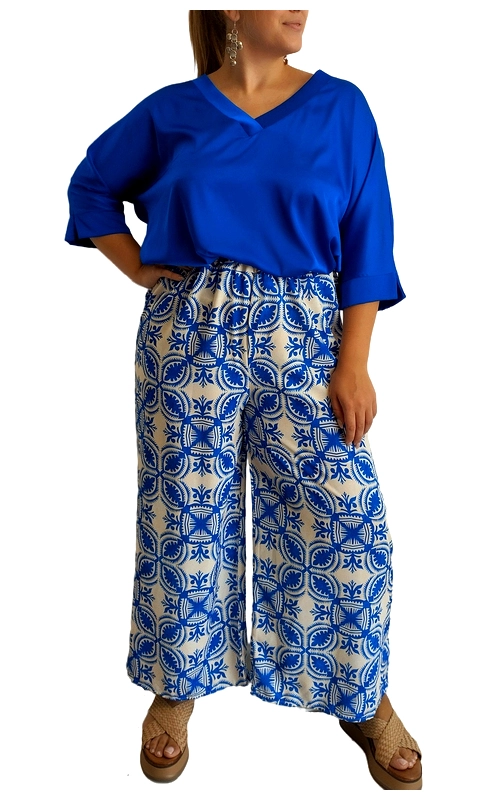 Κομψό σύνολο σε υπέροχες αποχρώσεις του μπλε ρουαγιάλ που αναδεικνύει τη θηλυκότητα και την άνεση. Η μπλούζα με V\u002Dλαιμόκοψη και φαρδιά τρία\u002Dτέταρτα μανίκια προσφέρει άνετη εφαρμογή και κομψή εμφάνιση. Συνδυάζεται αρμονικά με την εντυπωσιακή παντελόνα σε λευκό φόντο με έντονο μοτίβο σε μπλε ρουαγιάλ, εμπνευσμένο από παραδοσιακά μεσογειακά σχέδια. Η παντελόνα διαθέτει φαρδιά γραμμή που κολακεύει κάθε σωματότυπο και χαρίζει άνεση κατά την κίνηση. Ιδανικό για καλοκαιρινές βραδινές εξόδους, κοκτέιλ πάρτι ή ακόμα και για μια κομψή εμφάνιση στο γραφείο. Μπορεί να συνδυαστεί με επίπεδα σανδάλια για καθημερινές εμφανίσεις ή με ψηλοτάκουνα για πιο επίσημες περιστάσεις. Τα διακριτικά κοσμήματα αναδεικνύουν την κομψότητα του συνόλου. Η ποιότητα του υφάσματος εγγυάται άνεση καθ\u0027 όλη τη διάρκεια της ημέρας, ενώ το ζωντανό μοτίβο θα σας κάνει να ξεχωρίζετε με στυλ και αυτοπεποίθηση.