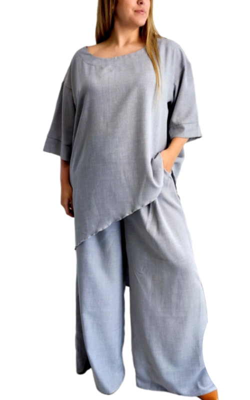 Αυτό το κομψό σετ σε απαλό γκρι\u002Dγαλάζιο (σταχτί) χρώμα αποτελεί την τέλεια επιλογή για γυναίκες που αναζητούν άνεση χωρίς να θυσιάζουν το στυλ. Η ασύμμετρη μπλούζα με το φαρδύ σχέδιο διαθέτει μια ιδιαίτερη διαγώνια γραμμή στο τελείωμα που προσδίδει μοντέρνα πινελιά, ενώ τα φαρδιά μανίκια 3/4 συμπληρώνουν την αέρινη σιλουέτα. Συνδυάζεται με φαρδύ παντελόνι στο ίδιο χρώμα και υλικό, δημιουργώντας ένα εντυπωσιακό σύνολο που κολακεύει κάθε σωματότυπο. Κατασκευασμένο από μαλακό, αναπνεύσιμο ύφασμα που μοιάζει με λινό, αυτό το σετ είναι ιδανικό για άνετες καθημερινές εμφανίσεις αλλά και για πιο κομψές περιστάσεις. Οι τσέπες στην μπλούζα προσθέτουν πρακτικότητα, ενώ η χαλαρή γραμμή του παντελονιού εξασφαλίζει άνεση όλη μέρα. Φορέστε το με απλά αξεσουάρ για καθημερινές εξόδους ή αναβαθμίστε το με κοσμήματα και κομψά παπούτσια για βραδινές εμφανίσεις. Ένα διαχρονικό κομμάτι που συνδυάζει την κομψότητα με την άνεση και προσαρμόζεται εύκολα σε κάθε γυναικεία γκαρνταρόμπα.