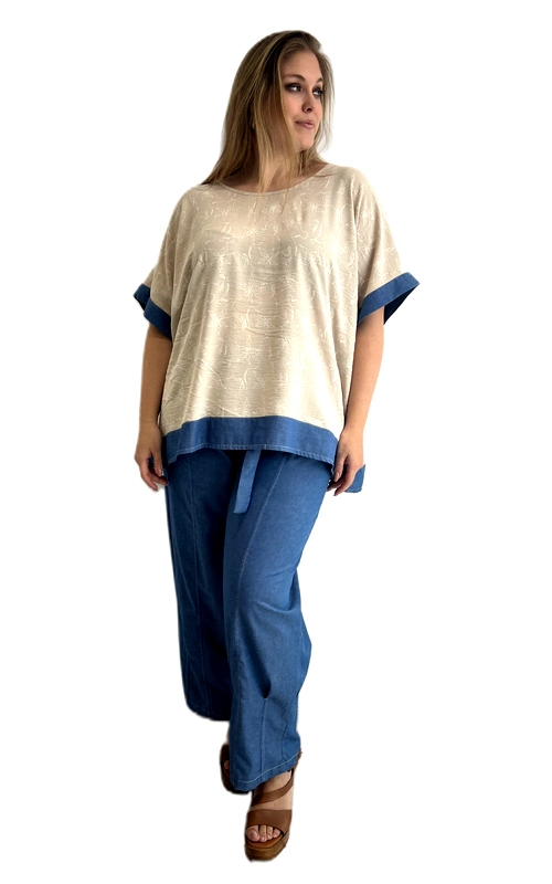 Μια μπλούζα που συνδυάζει άνεση και στυλ, ιδανική για τη σύγχρονη γυναίκα με καμπύλες. Σε κρεμ απόχρωση με λεπτό ανάγλυφο μοτίβο στο ύφασμα, η μπλούζα αυτή ξεχωρίζει χάρη στις εντυπωσιακές λεπτομέρειες της σε denim μπλε χρώμα, που διακρίνονται στο τελείωμα των μανικιών και στο κάτω μέρος του ρούχου. Η ευρύχωρη, oversized γραμμή της εξασφαλίζει μέγιστη άνεση, ενώ η στρογγυλή λαιμόκοψη προσφέρει κομψή και καθαρή εμφάνιση. Η βαριά, ποιοτική υφή του υφάσματος δίνει στο ρούχο μια πλούσια αίσθηση, ενώ η ασύμμετρη γραμμή του hem προσθέτει μοντέρνο χαρακτήρα. Μπορεί να φορεθεί με φαρδιά παντελόνα σε denim μπλε για ένα ολοκληρωμένο σύνολο, όπως φαίνεται στη φωτογραφία, αλλά και με λευκό παντελόνι ή φούστα για πιο ανάλαφρη εμφάνιση. Κατάλληλη για καθημερινές εξόδους, ψώνια ή χαλαρές συναντήσεις με φίλους, αυτή η μπλούζα αποτελεί must\u002Dhave κομμάτι για κάθε γυναικεία γκαρνταρόμπα plus size.