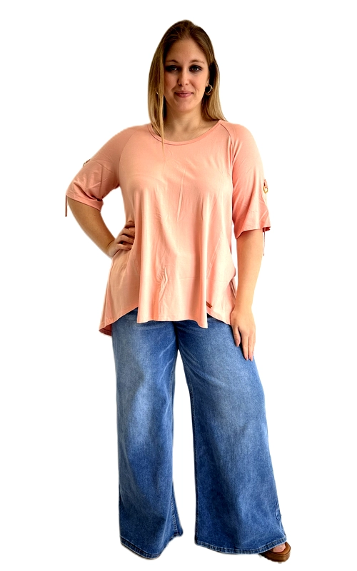 Η κοντομάνικη μπλούζα αυτή σε ζεστό ροδακινί χρώμα είναι η ιδανική επιλογή για κάθε γυναίκα που αναζητά άνεση και στυλ. Η χαλαρή, ευρύχωρη εφαρμογή της τη καθιστά ιδιαίτερα κολακευτική για plus size σιλουέτες, ενώ το ασύμμετρο τελείωμα στο κάτω μέρος προσθέτει μια μοντέρνα πινελιά. Το στρογγυλό ντεκολτέ και τα μανίκια ¾ με το ιδιαίτερο άνοιγμα στον αγκώνα, διακοσμημένα με μεταλλικά κρικάκια και λεπτό κορδόνι, αποτελούν το πιο εντυπωσιακό χαρακτηριστικό της μπλούζας. Η ραφή στο μπροστινό μέρος δίνει έναν ελαφρώς δομημένο χαρακτήρα, ενώ το απαλό, ελαστικό ύφασμα εξασφαλίζει άριστη εφαρμογή καθ\u0027 όλη τη διάρκεια της ημέρας. Μπορεί να συνδυαστεί υπέροχα με φαρδιά τζιν παντελόνια σε γαλάζιο denim, όπως στην εικόνα, αλλά και με κολάν ή casual παντελόνια για μια ολοκληρωμένη, άνετη εμφάνιση. Ιδανική για καθημερινές εξόδους, καφέ με φίλες ή ανοιξιάτικες βόλτες.
