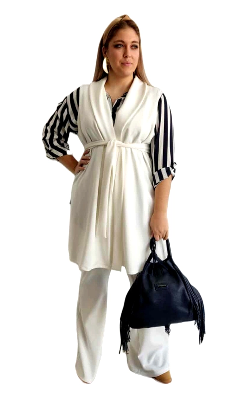 Κομψό γυναικείο γιλέκο σε λευκό ιβουάρ με μοντέρνα γραμμή που αναδεικνύει τη σιλουέτα. Διαθέτει φαρδύ γιακά και ζώνη στη μέση που δένει μπροστά, προσφέροντας έναν θηλυκό τόνο και δυνατότητα προσαρμογής στις διαστάσεις σας. Το μακρύ μήκος του το καθιστά ιδανικό για layering πάνω από ποικιλία ρούχων, όπως το εικονιζόμενο σύνολο με το ριγέ ασπρόμαυρο πουκάμισο και το λευκό παντελόνι. Το γιλέκο είναι κατασκευασμένο από ρέουσα, υψηλής ποιότητας ύφασμα που χαρίζει άνεση και κομψότητα σε κάθε κίνηση. Μπορεί να φορεθεί τόσο σε επαγγελματικές συναντήσεις όσο και σε βραδινές εξόδους, συνδυασμένο με τζιν για πιο casual εμφάνιση ή με κομψά παντελόνια για επίσημες περιστάσεις. Αποτελεί ένα ευέλικτο κομμάτι που θα αναβαθμίσει κάθε σας εμφάνιση, ενώ συνδυάζεται τέλεια με αξεσουάρ όπως η κομψή μαύρη τσάντα με τα κρόσσια που ολοκληρώνει το look.