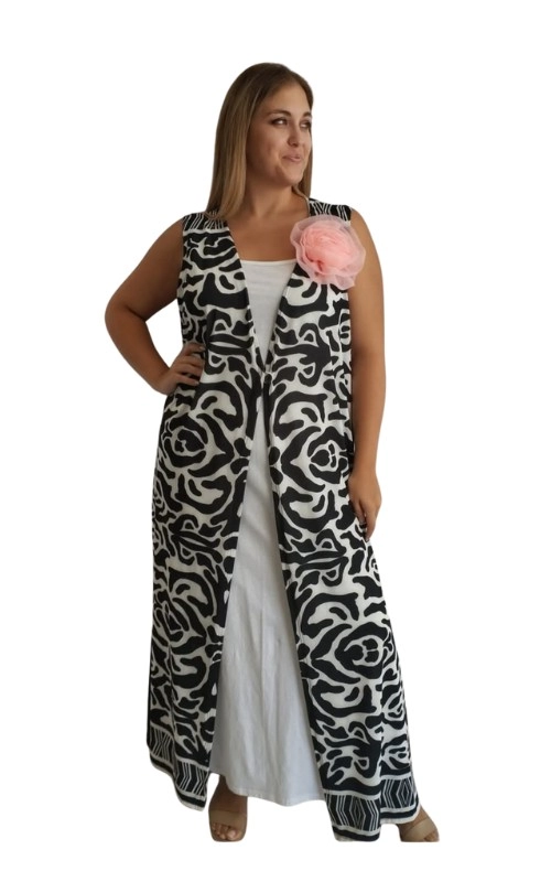 Αυτό το εντυπωσιακό μακρύ γιλέκο σε ασπρόμαυρο μοτίβο αποτελεί μια κομψή προσθήκη στη γκαρνταρόμπα σας. Με το χαρακτηριστικό γεωμετρικό σχέδιο που θυμίζει αφηρημένα λουλούδια σε μαύρο και λευκό χρώμα, το γιλέκο προσφέρει μια δυναμική αντίθεση που τραβάει αμέσως την προσοχή. Το αέρινο ύφασμα πέφτει χαλαρά στο σώμα, δημιουργώντας μια κολακευτική σιλουέτα που ταιριάζει σε διάφορους σωματότυπους. Ξεχωρίζει για το διακοσμητικό ροζ λουλούδι στον ώμο, προσθέτοντας μια θηλυκή, ρομαντική πινελιά στο γεωμετρικό σχέδιο. Φορέστε το πάνω από ένα απλό λευκό φόρεμα όπως στην εικόνα, ή συνδυάστε το με μονόχρωμα ρούχα για καθημερινές εμφανίσεις με στυλ. Ιδανικό για καλοκαιρινές βραδινές εξόδους, επίσημες περιστάσεις ή ακόμα και για το γραφείο όταν θέλετε να αναβαθμίσετε την εμφάνισή σας. Το μήκος του φτάνει μέχρι τον αστράγαλο, προσφέροντας κομψότητα και άνεση σε κάθε σας κίνηση.