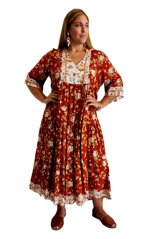 Ένα υπέροχο boho φόρεμα σε πλούσιο κεραμιδί χρώμα, διακοσμημένο με ρομαντικό floral μοτίβο από λευκά και μελί άνθη που απλώνονται σε όλη την επιφάνεια. Το σχέδιό του συνδυάζει ιδανικά τη θηλυκότητα με την άνεση, κάνοντάς το ιδανική επιλογή για κάθε plus size γυναίκα που θέλει να αναδείξει τη φιγούρα της με στυλ. Διαθέτει κομψό V\u002Dλαιμόκοψη με λευκή δαντέλα και διακοσμητικά στοιχεία στο μπούστο, ενώ η γραμμή empire δημιουργεί κολακευτική εφαρμογή. Οι βολάν στρώσεις στη φούστα και τα μανίκια με δαντελένια τελείωση προσδίδουν ρομαντική και αέρινη διάθεση. Το midi μήκος του εξασφαλίζει κομψή εμφάνιση, ενώ το ελαφρύ ύφασμα το κάνει ιδανικό για ζεστές μέρες. Μπορεί να φορεθεί σε καλοκαιρινές εκδρομές, σε beach parties, σε casual γεύματα αλλά και σε πιο επίσημες περιστάσεις. Συνδυάστε το με σανδάλια και statement σκουλαρίκια για ένα ολοκληρωμένο, boho\u002Dchic look που θα τραβήξει όλα τα βλέμματα.