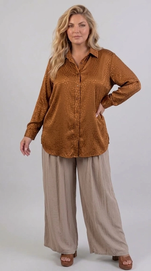 Κομψή γυναικεία πουκαμίσα plus size σε πλούσια απόχρωση καφέ\u002Dκονιάκ, με λεπτό jacquard μοτίβο που θυμίζει animal print λεοπάρ. Η σατέν υφή της υφής της προσδίδει ένα ιδιαίτερο λάμψιμο που την κάνει να ξεχωρίζει, ενώ παράλληλα παραμένει διακριτικά κομψή και εκλεπτυσμένη. Το oversized κόψιμό της εξασφαλίζει άνετη εφαρμογή, ιδανική για curvy σιλουέτες, ενώ το κλασικό γιακαδάκι και τα μακριά μανίκια της προσθέτουν έναν αέρα κλασικής κομψότητας. Η στρογγυλεμένη γραμμή στο τελείωμα της δίνει ένα μοντέρνο και χαλαρό ύφος. Μπορεί να φορεθεί με φαρδιά παντελόνα σε μπεζ ή εκρού τόνους για ένα αρμονικό αποτέλεσμα, όπως φαίνεται στο styling της φωτογραφίας. Εναλλακτικά, συνδυάζεται υπέροχα με τζιν ή δερμάτινο παντελόνι για ένα πιο δυναμικό look. Κατάλληλη για επαγγελματικές συναντήσεις, ρομαντικά ραντεβού ή βραδινές εξόδους, αυτή η πουκαμίσα αποτελεί must\u002Dhave κομμάτι για κάθε γυναικεία γκαρνταρόμπα.