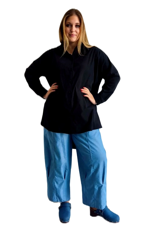 Η γυναικεία πουκαμίσα plus size σε βαθύ μαύρο χρώμα αποτελεί ένα διαχρονικό και ευέλικτο κομμάτι που κάθε γυναίκα πρέπει να έχει στη γκαρνταρόμπα της. Με το κλασικό γιακαδάκι και το κουμπάρισμα μπροστά, το σχέδιό της παραμένει απλό και κομψό, χωρίς περιττές λεπτομέρειες που να αποσπούν την προσοχή. Η oversized εφαρμογή της προσφέρει άνεση και ελευθερία κινήσεων, ενώ το μακρύ μανίκι και το επιμηκυμένο μήκος τη καθιστούν ιδανική για διάφορες περιστάσεις. Μπορεί να φορεθεί με φαρδιά παντελόνια σε γαλάζιο χρώμα, όπως φαίνεται στην εικόνα, για ένα σύγχρονο και χαλαρό look, αλλά και με στενό τζιν ή κολάν για πιο καθημερινό στυλ. Η ευέλικτη γραμμή της την κάνει κατάλληλη τόσο για επαγγελματικές όσο και για καθημερινές εξόδους. Ιδανική επιλογή για γυναίκες που αναζητούν στυλ και άνεση σε ένα μόνο κομμάτι.