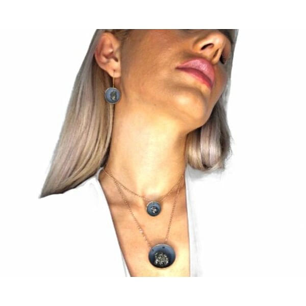 Κρεμαστά σκουλαρίκια με πυρίτη γκρι - 11214, Κρεμαστά σκουλαρίκια με πυρίτη γκρι που συνδυάζουν την κομψότητα με την μοντέρνα αισθητική, δημιουργώντας ένα μοναδικό κόσμημα για κάθε περίσταση. Σχεδιασμένα από την Ελληνίδα Σχεδιάστρια Κοσμημάτων Αικατερίνη Χαλκιαδάκη, αυτά τα χειροποίητα σκουλαρίκια διακρίνονται για την ιδιαίτερη γκρι απόχρωσή τους που θυμίζει χρώμα κιμωλίας.
Κατασκευασμένα από υψηλής ποιότητας ορείχαλκο, τα σκουλαρίκια φέρουν εντυπωσιακές πέτρες σιδηροπυρίτη που προσδίδουν μια φυσική και εκλεπτυσμένη αίσθηση. Η κυκλική φόρμα τους σε συνδυασμό με το ματ φινίρισμα δημιουργεί ένα statement κόσμημα που συμπληρώνει τόσο καθημερινές όσο και επίσημες εμφανίσεις. Το κλείσιμο με κρίκο εξασφαλίζει άνεση και ασφάλεια κατά τη χρήση.
Αυτά τα μοντέρνα σκουλαρίκια είναι ιδανικά για γυναίκες που αναζητούν πρωτότυπα χειροποίητα κοσμήματα με χαρακτήρα. Η ουδέτερη γκρι απόχρωση τους καθιστά εύκολα συνδυάσιμα με κάθε ντύσιμο, ενώ η ποιότητα κατασκευής εγγυάται μακροχρόνια χρήση. Αποθηκεύστε σε στεγνό χώρο και καθαρίστε με μαλακό πανί.