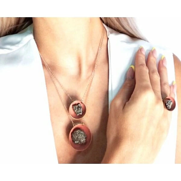 Γυναικείo κολιέ με πυρίτη - small somon - 10717, Ανακαλύψτε τη μαγεία του σιδηροπυρίτη με αυτό το εντυπωσιακό γυναικείο κολιέ που συνδυάζει την κομψότητα με την ιδιαίτερη φυσική ομορφιά. Σχεδιασμένο από την Ελληνίδα Σχεδιάστρια Κοσμημάτων Αικατερίνη Χαλκιαδάκη, αυτό το μοναδικό χειροποίητο κόσμημα αποτελεί την ιδανική επιλογή για γυναίκες που αγαπούν τα statement αξεσουάρ.
Το κολιέ διαθέτει μια εντυπωσιακή οβάλ πέτρα σιδηροπυρίτη σε υπέροχη σομόν απόχρωση, η οποία συνδυάζεται αρμονικά με τον ορείχαλκο. Η φυσική λάμψη του πυρίτη δημιουργεί παιχνίδια φωτός που προσδίδουν εκλεπτυσμένη αίσθηση στο κόσμημα. Η λεπτή αλυσίδα από ορείχαλκο ολοκληρώνει τον σχεδιασμό, προσφέροντας άνεση και κομψότητα.
Αυτό το χειροποίητο κολιέ με πυρίτη αποτελεί την τέλεια συμπλήρωση για καθημερινές και ιδιαίτερες εμφανίσεις. Η ουδέτερη σομόν απόχρωση το καθιστά εύκολα συνδυάσιμο με κάθε ντυσίματος, ενώ η μοναδική υφή του πυρίτη προσθέτει έναν εντυπωσιακό χαρακτήρα.