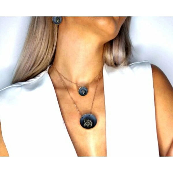 Μεγάλο κολιέ μακρύ με πυρίτη γκρι - 10868, Ανακαλύψτε το μοναδικό χειροποίητο κολιέ με πυρίτη που συνδυάζει τη φυσική ομορφιά του σιδηροπυρίτη με τη σύγχρονη ελληνική αισθητική. Αυτό το εντυπωσιακό μακρύ κολιέ, σχεδιασμένο από την Αικατερίνη Χαλκιαδάκη, αποτελεί την ιδανική επιλογή για γυναίκες που αναζητούν statement κοσμήματα με φυσικές πέτρες.
Το κολιέ διακρίνεται για τον μοναδικό συνδυασμό υλικών και χρωμάτων. Η κεντρική κρεμαστή ενότητα παρουσιάζει έναν γκρι δίσκο από ρητίνη με χρώμα κιμωλίας, που φιλοξενεί έναν λαμπερό σιδηροπυρίτη με μεταλλικές ανταύγειες. Η ορειχάλκινη βάση και αλυσίδα προσφέρουν ανθεκτικότητα και χρυσαφένια απόχρωση που συμπληρώνει αρμονικά τους γήινους τόνους της πέτρας.