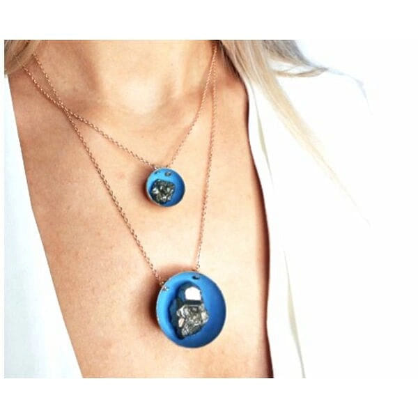 Μεγάλο κολιέ μακρύ με πυρίτη μπλε - 10812, Ανακαλύψτε τη μαγεία του μεγάλου μακρύ κολιέ με πυρίτη σε εντυπωσιακό μπλε χρώμα, ένα statement κόσμημα που συνδυάζει την ελληνική τέχνη με τη σύγχρονη αισθητική. Σχεδιασμένο από την Ελληνίδα Σχεδιάστρια Κοσμημάτων Αικατερίνη Χαλκιαδάκη, αυτό το χειροποίητο κολιέ εντυπωσιάζει με την ιδιαίτερη γεωμετρική του φόρμα και τον φυσικό σιδηροπυρίτη που λάμπει στο κέντρο του.
Το κολιέ διαθέτει μεγάλο στρογγυλό pendant από ρητίνη σε γαλάζια απόχρωση που περιβάλλει τον φυσικό πυρίτη, δημιουργώντας μια εντυπωσιακή σύνθεση που τραβά τα βλέμματα. Ο συνδυασμός του ορείχαλκου με τις αποχρώσεις του μπλε και της κιμωλίας προσφέρει μια κομψή και μοντέρνα αισθητική που ταιριάζει τέλεια σε layering looks ή μόνο του ως statement piece.