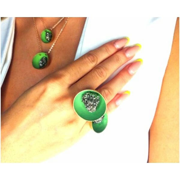 Μεγάλο εντυπωσιακό δαχτυλίδι με διπλό πυρίτη πράσινο - 10972, Ανακαλύψτε τη μαγεία του χειροποίητου κοσμήματος με αυτό το εντυπωσιακό δαχτυλίδι που φέρει διπλό σιδηροπυρίτη σε πράσινες αποχρώσεις. Σχεδιασμένο από την Ελληνίδα Σχεδιάστρια Κοσμημάτων Αικατερίνη Χαλκιαδάκη, αυτό το μοναδικό κόσμημα συνδυάζει την ελληνική τεχνογνωσία με τη σύγχρονη αισθητική.
Το δαχτυλίδι διαθέτει δύο στρογγυλές επιφάνειες διαφορετικών διαστάσεων, κατασκευασμένες από ποιοτικό ορείχαλκο με μαύρη πατίνα που δημιουργεί εντυπωσιακές αντιθέσεις. Κάθε επιφάνεια φιλοξενεί έναν λαμπερό σιδηροπυρίτη, γνωστό και ως "χρυσάφι του ανόητου", που δημιουργεί μαγευτικούς χρυσαφένιους αντανακλασμούς μέσα στη ρητίνη πράσινου χρώματος.
Η ανατομική σχεδίαση του δαχτυλιδιού εξασφαλίζει άνετη εφαρμογή, ενώ το statement design το καθιστά ιδανικό για όσες αγαπούν τα εντυπωσιακά κοσμήματα. Συνδυάζεται τέλεια με casual και επίσημα outfits, προσδίδοντας μια bohemian πινελιά στη διάθεσή σας.