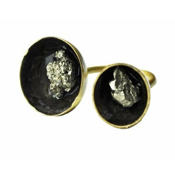 Ανακαλύψτε την τέλεια ισορροπία μεταξύ δύναμης και κομψότητας με αυτό το μεγάλο εντυπωσιακό γυναικείο δαχτυλίδι με διπλό πυρίτη, σχεδιασμένο από την Αικατερίνη Χαλκιαδάκη. Το μοναδικό χειροποίητο δαχτυλίδι συνδυάζει δύο φυσικούς κρυστάλλους σιδηροπυρίτη σε μια εκπληκτική σύνθεση που κεντρίζει τα βλέμματα.\u000AΗ μαύρη πατίνα δημιουργεί εντυπωσιακή αντίθεση με τα χρυσαφί κρύσταλλα του πυρίτη, ενώ ο ορείχαλκος προσδίδει θερμότητα και διαρκότητα στο κόσμημα. Η ανοιχτή δομή του δαχτυλιδιού επιτρέπει την άνετη εφαρμογή σε διάφορα μεγέθη δακτύλου, ενώ οι δύο ωοειδείς πέτρες πυρίτη σε διαφορετικά μεγέθη δημιουργούν δυναμική σύνθεση.\u000AΟ σιδηροπυρίτης, γνωστός και ως \u0022χρυσός των ανόητων\u0022, θεωρείται πέτρα προστασίας και δύναμης, ιδανική για γυναίκες που θέλουν να εκφράσουν την προσωπικότητά τους με στυλ. Το statement δαχτυλίδι συνδυάζεται τέλεια με casual και επίσημα outfits, προσδίδοντας μοναδικό χαρακτήρα σε κάθε εμφάνιση.