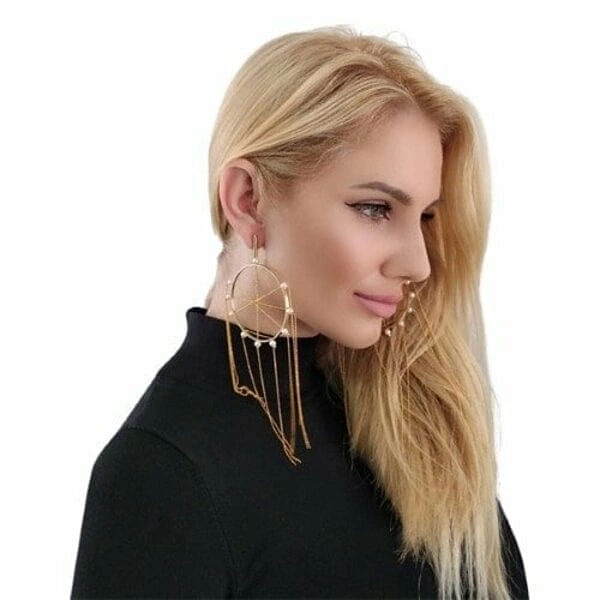 Μεγάλα εντυπωσιακά σκουλαρίκια κρεμαστά με πέρλες - 2970, Ανακαλύψτε τη μαγεία των μεγάλων εντυπωσιακών σκουλαρικιών κρεμαστών με πέρλες που θα μεταμορφώσουν κάθε σας εμφάνιση. Αυτά τα μοναδικά χειροποίητα σκουλαρίκια "Ονειροπαγίδα", σχεδιασμένα από την Ελληνίδα Σχεδιάστρια Κοσμημάτων Αικατερίνη Χαλκιαδάκη, συνδυάζουν τη σύγχρονη αισθητική με την παραδοσιακή ελληνική τεχνοτροπία.
Κατασκευασμένα από υψηλής ποιότητας ορείχαλκο με χρυσή απόχρωση, τα σκουλαρίκια διαθέτουν γεωμετρικό σχέδιο κύκλων που στολίζονται με φυσικές πέρλες. Οι κρεμαστές αλυσίδες δημιουργούν μια κομψή κίνηση που προσελκύει τα βλέμματα, ενώ το statement design τους τα καθιστά ιδανικά για ιδιαίτερες στιγμές.
Τα μακριά σκουλαρίκια συνδυάζονται τέλεια με βραδινά σύνολα, νυφικές εμφανίσεις ή boho chic looks, προσφέροντας μια πινελιά πολυτέλειας και μυστηρίου. Η εργονομική τους κατασκευή εξασφαλίζει άνεση όλη μέρα.