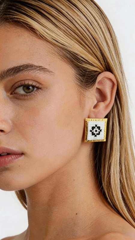 Κεντητά σκουλαρίκια statement με γεωμετρικά σχέδια από χρυσοκλωστή σε άσπρο - SKOUL-4716 | Candiashop Boutique, Τα κεντητά σκουλαρίκια statement με γεωμετρικά σχέδια από χρυσοκλωστή σε άσπρο αποτελούν την τέλεια επιλογή για τη γυναίκα που αναζητά εντυπωσιακά και μοντέρνα κοσμήματα. Σχεδιασμένα από την Ελληνίδα Σχεδιάστρια Κοσμημάτων Αικατερίνη Χαλκιαδάκη, συνδυάζουν την παραδοσιακή τέχνη του κεντήματος με σύγχρονη αισθητική. Κάθε σκουλαρίκι διαθέτει τετράγωνη φόρμα με εκλεπτυσμένο γεωμετρικό μοτίβο κεντημένο με χρυσοκλωστή σε λευκή βάση. Το folklore design δημιουργεί μια μοναδική αντίθεση που προσδίδει κομψότητα και χαρακτήρα σε κάθε εμφάνιση. Τα χειροποίητα σκουλαρίκια είναι ιδανικά για γάμο, ειδικές εκδηλώσεις ή ως καθημερινό statement κόσμημα. Η υψηλή ποιότητα κατασκευής και τα επιλεγμένα υλικά εγγυώνται ανθεκτικότητα και άνεση στη χρήση. Το ελαφρύ τους βάρος τα καθιστά κατάλληλα για όλη τη μέρα, ενώ το μέγεθός τους προσδίδει τη σωστή δόση glamour χωρίς υπερβολή. Υλικό: Ορείχαλκος, Ύφασμα Φροντίστε τα σκουλαρίκια σας αποφεύγοντας την επαφή με νερό και αρώματα. Φυλάσσετε τα σε στεγνό μέρος για να διατηρήσουν τη λάμψη τους.