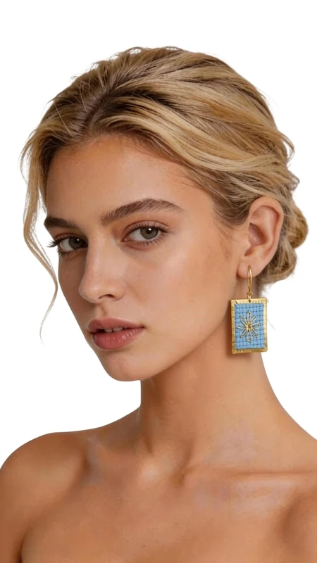 Τα statement κεντητά σκουλαρίκια με γεωμετρικά σχέδια από χρυσοκλωστή σε γαλάζιο αποτελούν έναν μοναδικό συνδυασμό παραδοσιακής τέχνης και μοντέρνου σχεδιασμού. Σχεδιασμένα από την Ελληνίδα Σχεδιάστρια Κοσμημάτων Αικατερίνη Χαλκιαδάκη, αυτά τα εντυπωσιακά χειροποίητα σκουλαρίκια αναδεικνύουν την κομψότητα κάθε look με στιλ και χαρακτήρα. Η λεπτή κεντητική τεχνική με χρυσοκλωστή δημιουργεί ένα υπέροχο αποτέλεσμα που λαμπυρίζει διακριτικά, ενώ το γαλάζιο χρώμα προσφέρει μια φρεσκάδα που ταιριάζει τέλεια με θερινά και καλοκαιρινά outfit. Τα γεωμετρικά σχέδια προσδίδουν μοντέρνα αισθητική, κάνοντας τα εντυπωσιακά σκουλαρίκια ιδανική επιλογή για κάθε περίσταση. Τα χειροποίητα κεντητά σκουλαρίκια είναι τέλεια για γάμους, βαφτίσια, καλοκαιρινά πάρτι και κάθε ειδική στιγμή όπου θέλετε να ξεχωρίσετε. Συνδυάστε τα με λευκό ή μπλε ρούχα για να αναδείξετε το γαλάζιο τους χρώμα. Υλικό: Ορείχαλκος, Ύφασμα Φροντίστε τα σκουλαρίκια σας αποθηκεύοντάς τα σε στεγνό μέρος, μακριά από υγρασία και άμεση ηλιακή ακτινοβολία για να διατηρήσουν τη λάμψη τους.