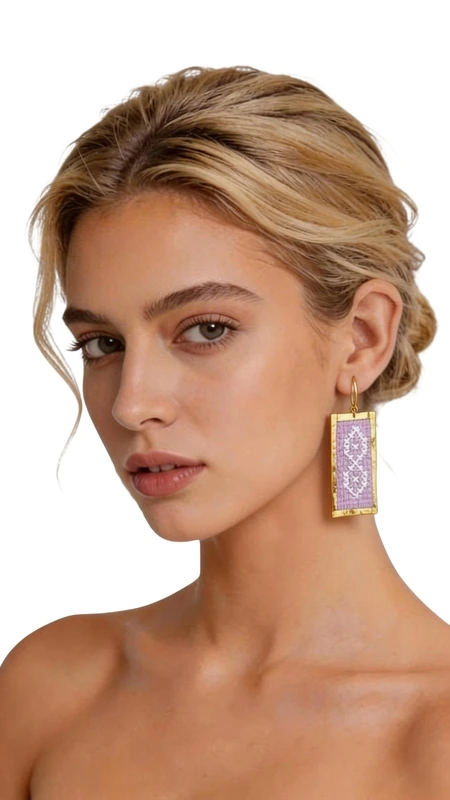 Τα statement σκουλαρίκια με κεντητά γεωμετρικά σχέδια από χρυσοκλωστή σε λιλά χρώμα είναι η τέλεια επιλογή για γυναίκες που αγαπούν τα εντυπωσιακά και πρωτότυπα κοσμήματα. Σχεδιασμένα από την Ελληνίδα Σχεδιάστρια Κοσμημάτων Αικατερίνη Χαλκιαδάκη, αυτά τα χειροποίητα σκουλαρίκια συνδυάζουν την παραδοσιακή τέχνη του κεντήματος με σύγχρονο design. Κάθε σκουλαρίκι δημιουργείται με ιδιαίτερη προσοχή στη λεπτομέρεια, χρησιμοποιώντας χρυσοκλωστή που σχηματίζει υπέροχα γεωμετρικά μοτίβα σε απαλό λιλά χρώμα. Η ορθογώνια φόρμα και το κρεμαστό στυλ τους τα καθιστούν ιδανικά για κάθε περίσταση, από καθημερινά outfit έως ειδικές εμφανίσεις και γαμήλιες εκδηλώσεις. Τα κεντητά σκουλαρίκια προσφέρουν μοναδική αίσθηση κομψότητας και στυλ, ενώ η ελαφριά τους κατασκευή εξασφαλίζει άνετη χρήση όλη την ημέρα. Το folklore design τους αντικατοπτρίζει την ελληνική παράδοση σε μοντέρνο ύφος. Υλικό: Ορείχαλκος, Ύφασμα Φροντίστε τα απαλά με στεγνό πανί και αποθηκεύστε τα σε ασφαλές μέρος για να διατηρήσουν την ομορφιά τους.