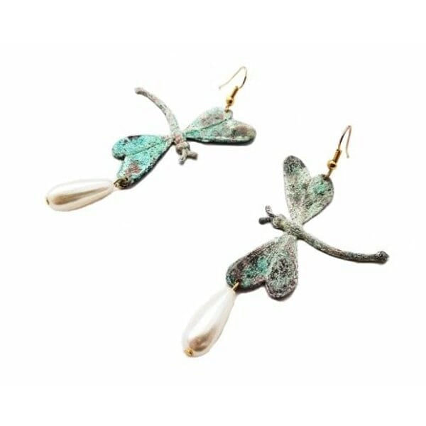 Ανακαλύψτε τη μαγεία της φύσης με αυτά τα εντυπωσιακά κρεμαστά σκουλαρίκια λιβελούλες, σχεδιασμένα από την Ελληνίδα Σχεδιάστρια Κοσμημάτων Αικατερίνη Χαλκιαδάκη. Τα μοναδικά αυτά χειροποίητα κοσμήματα συνδυάζουν την κομψότητα των φυσικών μαργαριταριών με τη βοημιακή αισθητική του οξειδωμένου ορείχαλκου.\u000AΚάθε λιβελούλα έχει δημιουργηθεί με απόλυτη προσοχή στη λεπτομέρεια, παρουσιάζοντας υπέροχες αποχρώσεις πράσινου που δημιουργούν μια vintage patina επίδραση. Οι φυσικές πέρλες που κρέμονται κομψά στο κάτω μέρος προσδίδουν μια αίσθηση luxury και θηλυκότητας, ενώ ο χειροποίητος χαρακτήρας κάνει κάθε ζευγάρι μοναδικό.\u000AΑυτά τα statement σκουλαρίκια είναι ιδανικά για ιδιαίτερες περιστάσεις, boho chic εμφανίσεις ή ως το τέλειο νυφικό αξεσουάρ για μια εναλλακτική νύφη που αγαπά την πρωτοτυπία.