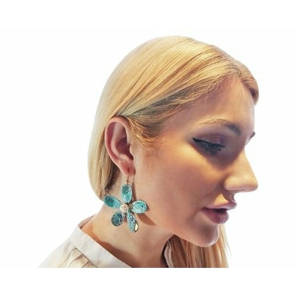 Μεγάλα εντυπωσιακά σκουλαρίκια κρεμαστά με πέρλες - 3005, Μεγάλα εντυπωσιακά κρεμαστά σκουλαρίκια με πέρλες που συνδυάζουν το boho στιλ με τη σύγχρονη αισθητική. Αυτά τα μοναδικά χειροποίητα γυναικεία σκουλαρίκια λουλούδια, σχεδιασμένα από την Ελληνίδα Σχεδιάστρια Κοσμημάτων Αικατερίνη Χαλκιαδάκη, ξεχωρίζουν για τη μοντέρνα patina επίστρωση που δημιουργεί εντυπωσιακούς πράσινους τόνους με χρυσαφένιες πινελιές.
Κάθε σκουλαρίκι διαμορφώνεται σε σχήμα μαργαρίτας με έξι οβάλ πέταλα από οξειδωμένο ορείχαλκο, ενώ στο κέντρο φιλοξενεί μία φυσική πέρλα που προσδίδει κομψότητα και φως. Η τεχνική του οξειδωμένου χαλκού δίνει μοναδικούς χρωματισμούς που κάνουν κάθε κόσμημα ξεχωριστό. Το μέγεθός τους καθιστά αυτά τα εντυπωσιακά σκουλαρίκια για γάμο ή ειδικές περιστάσεις την ιδανική επιλογή.
Ιδανικά για να συνδυαστούν με boho ντυσίματα ή να προσθέσουν χρώμα σε μονόχρωμα outfits.