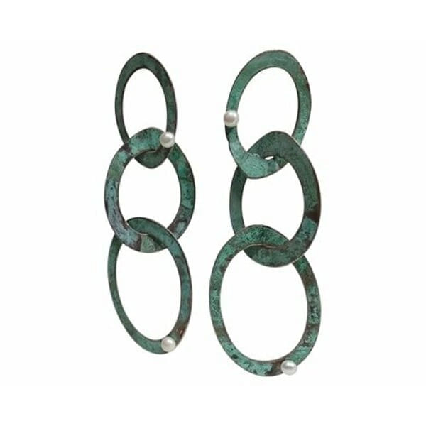 Ανακαλύψτε τη μαγεία των μεγάλων εντυπωσιακών σκουλαρικιών που συνδυάζουν την κομψότητα του χαλκού με την πράσινη πατίνα σε ένα μοναδικό design. Αυτά τα χειροποίητα μακριά καρφωτά σκουλαρίκια, σχεδιασμένα από την Ελληνίδα Σχεδιάστρια Κοσμημάτων Αικατερίνη Χαλκιαδάκη, δημιουργούν statement look που προσελκύει τα βλέμματα.\u000AΤο innovative design με τους αλληλένδετους κρίκους σε πράσινη πατίνα δίνει bohemian αισθητική που ταιριάζει τέλεια σε σύγχρονες γυναίκες. Κάθε κρίκος είναι χειροτεχνημένος από υψηλής ποιότητας χαλκό και διακοσμημένος με φυσικά μαργαριτάρια που προσθέτουν λάμψη και κομψότητα. Η μοναδική πράσινη πατίνα δημιουργεί vintage αίσθηση που συνδυάζεται άψογα με μοντέρνα και κλασικά outfits.\u000AΤα κρεμαστά σκουλαρίκια αυτά είναι ιδανικά για ιδιαίτερες στιγμές, νυφικές εμφανίσεις ή everyday chic looks. Η ελληνική τεχνογνωσία φαίνεται σε κάθε λεπτομέρεια, από την τέλεια ισορροπία των κρίκων μέχρι την προσεκτική τοποθέτηση των περλών. Φυλάξτε τα σε στεγνό μέρος και καθαρίστε τα απαλά με μαλακό πανί.