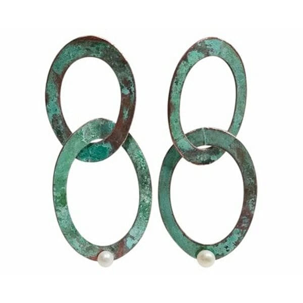 Αναδείξτε τη μοναδική σας προσωπικότητα με αυτά τα εντυπωσιακά μεγάλα σκουλαρίκια κρεμαστά που συνδυάζουν την κομψότητα των μαργαριταριών με τη μοντέρνα αισθητική του χαλκού. Σχεδιασμένα από την Ελληνίδα Σχεδιάστρια Κοσμημάτων Αικατερίνη Χαλκιαδάκη, αυτά τα χειροποίητα σκουλαρίκια φέρουν την υπογραφή της γνήσιας ελληνικής τέχνης κοσμηματοποιίας.\u000AΗ μοναδική πράσινη πατίνα που καλύπτει τους διπλούς κρίκους δημιουργεί ένα vintage αποτέλεσμα που συναρπάζει, ενώ οι φυσικές πέρλες προσθέτουν μια πινελιά κομψότητας και λάμψης. Κάθε κομμάτι είναι μοναδικό, καθώς η πατίνα αναπτύσσεται φυσικά στον χαλκό, δημιουργώντας ανεπανάληπτες αποχρώσεις και υφές.\u000AΤα μακριά αυτά σκουλαρίκια είναι ιδανικά για ιδιαίτερες εμφανίσεις, γάμους, βραδινές εξόδους ή όταν θέλετε να προσθέσετε μια boho πινελιά στο καθημερινό σας στυλ. Το ιδιαίτερο σχήμα των διπλών κρίκων δημιουργεί όμορφες κινήσεις και αντανακλάσεις φωτός.