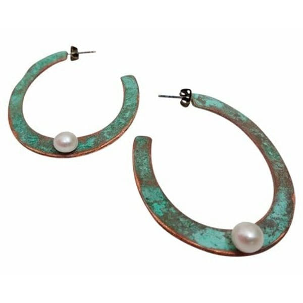Εντυπωσιακά σκουλαρίκια κρίκοι με μαργαριτάρια που συνδυάζουν τη φυσική ομορφιά του χαλκού με την κομψότητα των πέρλων. Αυτά τα μεγάλα καρφωτά σκουλαρίκια, σχεδιασμένα από την Ελληνίδα Σχεδιάστρια Κοσμημάτων Αικατερίνη Χαλκιαδάκη, διαθέτουν μοναδική πράσινη πατίνα που προσδίδει vintage χαρακτήρα και αυθεντικότητα.\u000AΚάθε σκουλαρίκι φέρει μία λευκή πέρλα τοποθετημένη στρατηγικά στο κάτω μέρος του κρίκου, δημιουργώντας ένα τέλειο contrast με την οξειδωμένη επιφάνεια του χαλκού. Η χειροποίητη κατασκευή και η φυσική πατίνα καθιστούν κάθε ζεύγος μοναδικό, ενώ ο ανοιχτός σχεδιασμός του κρίκου προσφέρει άνεση και στυλ.\u000AΙδανικά για γυναίκες που αγαπούν τα statement κοσμήματα με boho στοιχεία, αυτά τα σκουλαρίκια ολοκληρώνουν τόσο casual όσο και επίσημα looks. Η κλασική φόρμα του κρίκου σε συνδυασμό με την πέρλα τα καθιστά κατάλληλα για γάμους, ειδικές περιστάσεις και καθημερινή χρήση.