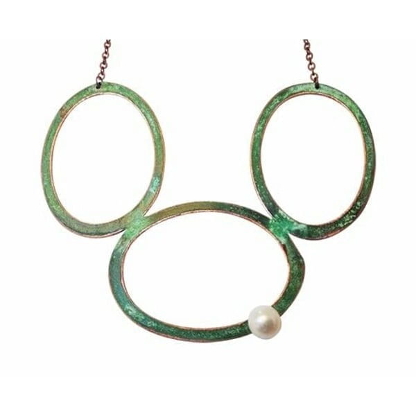 Ενα εντυπωσιακό μεγάλο γυναικείο κολιέ με μαργαριτάρι που συνδυάζει τη μοναδικότητα του χειροποίητου σχεδιασμού με την κομψότητα του οξειδωμένου χαλκού. Αυτό το statement κολιέ, σχεδιασμένο από την Αικατερίνη Χαλκιαδάκη, αποτελεί τη τέλεια επιλογή για γυναίκες που αναζητούν ένα ιδιαίτερο κόσμημα που θα τραβά τα βλέμματα.\u000AΤο μακρύ κολιέ διαθέτει τρεις μεγάλους κυκλικούς κρίκους από χαλκό με πράσινο patina φινίρισμα που δημιουργεί μια vintage αισθητική. Ένα φυσικό μαργαριτάρι κοσμεί έναν από τους κρίκους, προσθέτοντας λάμψη και κομψότητα στο σύνολο. Η μοναδική εμφάνιση του οξειδωμένου χαλκού καθιστά κάθε κολιέ μοναδικό, καθώς το patina αναπτύσσεται φυσικά με τον χρόνο.\u000AΙδανικό για layering με άλλα κοσμήματα ή ως αυτοτελές statement piece, αυτό το εντυπωσιακό κολιέ προσθέτει μια καλλιτεχνική πινελιά σε κάθε outfit. Η χειροποίητη κατασκευή εγγυάται την ποιότητα και τη μοναδικότητα του ελληνικού κοσμήματος.