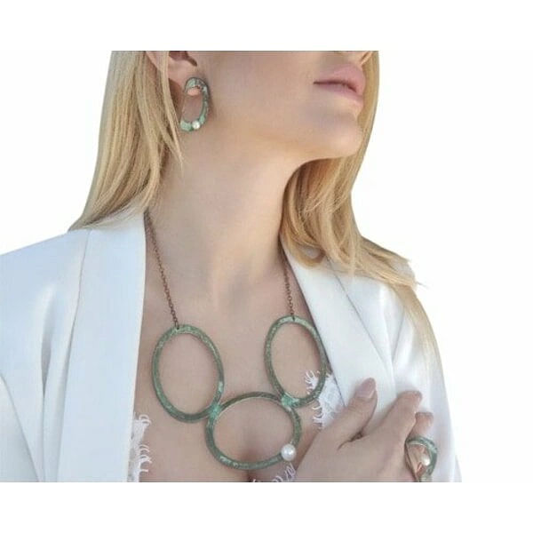 Μεγάλο γυναικείο κολιέ με μαργαριτάρι και χρώμα - 3046, Ενα εντυπωσιακό μεγάλο γυναικείο κολιέ με μαργαριτάρι που συνδυάζει τη μοναδικότητα του χειροποίητου σχεδιασμού με την κομψότητα του οξειδωμένου χαλκού. Αυτό το statement κολιέ, σχεδιασμένο από την Αικατερίνη Χαλκιαδάκη, αποτελεί τη τέλεια επιλογή για γυναίκες που αναζητούν ένα ιδιαίτερο κόσμημα που θα τραβά τα βλέμματα.
Το μακρύ κολιέ διαθέτει τρεις μεγάλους κυκλικούς κρίκους από χαλκό με πράσινο patina φινίρισμα που δημιουργεί μια vintage αισθητική. Ένα φυσικό μαργαριτάρι κοσμεί έναν από τους κρίκους, προσθέτοντας λάμψη και κομψότητα στο σύνολο. Η μοναδική εμφάνιση του οξειδωμένου χαλκού καθιστά κάθε κολιέ μοναδικό, καθώς το patina αναπτύσσεται φυσικά με τον χρόνο.
Ιδανικό για layering με άλλα κοσμήματα ή ως αυτοτελές statement piece, αυτό το εντυπωσιακό κολιέ προσθέτει μια καλλιτεχνική πινελιά σε κάθε outfit. Η χειροποίητη κατασκευή εγγυάται την ποιότητα και τη μοναδικότητα του ελληνικού κοσμήματος.
