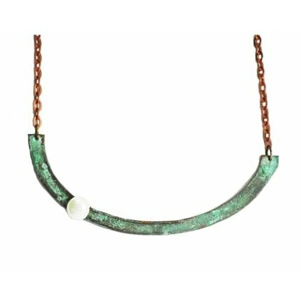Ανακαλύψτε τη μαγεία του χειροποίητου κοσμήματος με αυτό το εντυπωσιακό γυναικείο κολιέ σε σχήμα ημικύκλιου, σχεδιασμένο από την Ελληνίδα Σχεδιάστρια Κοσμημάτων Αικατερίνη Χαλκιαδάκη. Το μοναδικό αυτό statement κολιέ συνδυάζει τον οξειδωμένο χαλκό σε πράσινες αποχρώσεις με την κλασική κομψότητα του λευκού μαργαριταριού, δημιουργώντας ένα κόσμημα που ξεχωρίζει.\u000AΗ ημικυκλική σιλουέτα προσφέρει μοντέρνο στιλ και γεωμετρική αισθητική, ενώ το φυσικό patina του χαλκού σε πράσινες αποχρώσεις δίνει χαρακτήρα και αυθεντικότητα. Το λευκό μαργαριτάρι που διακοσμεί το κολιέ προσθέτει μια νότα κλασικής κομψότητας, δημιουργώντας την τέλεια αντίθεση με το οξειδωμένο μέταλλο.\u000AΙδανικό για layering με άλλα κολιέ ή ως αυτόνομο statement piece, αυτό το χειροποίητο κόσμημα μεταμορφώνει κάθε εμφάνιση από casual σε sophisticated. Η ανατομική του φόρμα εφαρμόζει άνετα στον λαιμό, ενώ η χάλκινη αλυσίδα εξασφαλίζει άνεση και στιλ.