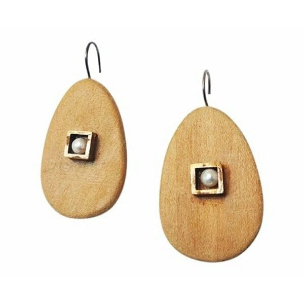 Ανακαλύψτε τη φυσική κομψότητα με αυτά τα μοναδικά κρεμαστά σκουλαρίκια που συνδυάζουν ξύλο και μαργαριτάρια σε έναν υπέροχο σχεδιασμό. Σχεδιασμένα από την Ελληνίδα Σχεδιάστρια Κοσμημάτων Αικατερίνη Χαλκιαδάκη, αυτά τα χειροποίητα κοσμήματα προσφέρουν μια σύγχρονη ματιά στην κλασική κομψότητα.\u000AΚάθε σκουλαρίκι χαρακτηρίζεται από μια οβάλ ξύλινη βάση σε φυσικό καφέ χρώμα που συμπληρώνεται από ένα τετράγωνο μεταλλικό στοιχείο με λευκή πέρλα στο κέντρο. Ο συνδυασμός αυτός δημιουργεί μια υπέροχη αντίθεση υφών και χρωμάτων που προσελκύει το βλέμμα. Η φυσική ζεστασιά του ξύλου αρμονίζει τέλεια με τη λάμψη των μαργαριταριών, δημιουργώντας ένα κόσμημα που είναι ιδανικό τόσο για καθημερινή όσο και για ειδική εμφάνιση.