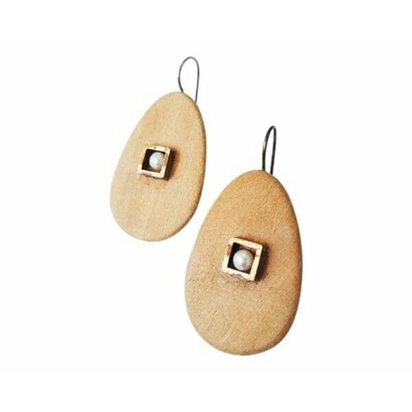 Σκουλαρίκια κρεμαστά με ξύλο και μαργαριτάρια - 3983, Ανακαλύψτε τη φυσική κομψότητα με αυτά τα μοναδικά κρεμαστά σκουλαρίκια που συνδυάζουν ξύλο και μαργαριτάρια σε έναν υπέροχο σχεδιασμό. Σχεδιασμένα από την Ελληνίδα Σχεδιάστρια Κοσμημάτων Αικατερίνη Χαλκιαδάκη, αυτά τα χειροποίητα κοσμήματα προσφέρουν μια σύγχρονη ματιά στην κλασική κομψότητα.
Κάθε σκουλαρίκι χαρακτηρίζεται από μια οβάλ ξύλινη βάση σε φυσικό καφέ χρώμα που συμπληρώνεται από ένα τετράγωνο μεταλλικό στοιχείο με λευκή πέρλα στο κέντρο. Ο συνδυασμός αυτός δημιουργεί μια υπέροχη αντίθεση υφών και χρωμάτων που προσελκύει το βλέμμα. Η φυσική ζεστασιά του ξύλου αρμονίζει τέλεια με τη λάμψη των μαργαριταριών, δημιουργώντας ένα κόσμημα που είναι ιδανικό τόσο για καθημερινή όσο και για ειδική εμφάνιση.