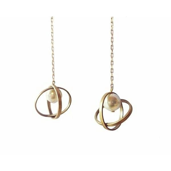 Χειροποίητα γυναικεία σκουλαρίκια κρεμαστά με πέρλες - 2982, Ανακαλύψτε τη μαγεία των χειροποίητων γυναικείων σκουλαρικιών με πέρλες που συνδυάζουν την κομψότητα με τη μοντέρνα αισθητική. Αυτά τα εντυπωσιακά κρεμαστά σκουλαρίκια, σχεδιασμένα από την Ελληνίδα Σχεδιάστρια Κοσμημάτων Αικατερίνη Χαλκιαδάκη, προσφέρουν έναν μοναδικό συνδυασμό γεωμετρικών σχημάτων και φυσικής ομορφιάς.
Η καινοτόμα σχεδίαση περιλαμβάνει περιστρεφόμενα δακτυλίδια από ορείχαλκο σε χρυσαφί απόχρωση που πλαισιώνουν λευκές πέρλες, δημιουργώντας μια δυναμική και σύγχρονη αισθητική. Η μακριά αλυσίδα προσθέτει κίνηση και κομψότητα, καθιστώντας τα ιδανικά για ειδικές περιστάσεις και καθημερινή φθορά.
Κατασκευασμένα με επιμέλεια από premium ορείχαλκο, αυτά τα statement σκουλαρίκια αντέχουν στον χρόνο διατηρώντας τη λάμψη τους. Ο συνδυασμός των φυσικών περιών με τα μεταλλικά στοιχεία δημιουργεί μια τέλεια ισορροπία μεταξύ κλασικού και μοντέρνου στυλ.