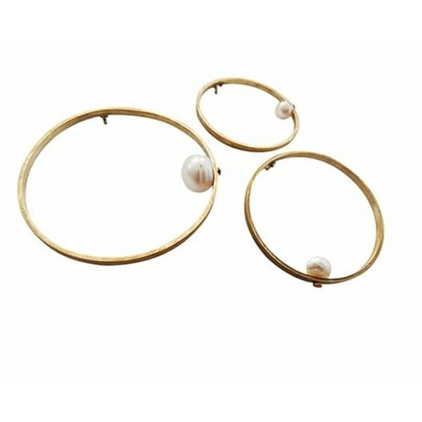 Γυναικείες καρφίτσες κόσμημα με πέρλες - 2979, Ανακαλύψτε τη μαγεία των χειροποίητων καρφιτσών με αυτό το εντυπωσιακό σετ τριών κυκλικών καρφιτσών από ορείχαλκο και φυσικές πέρλες. Κάθε καρφίτσα παρουσιάζει έναν κομψό κυκλικό σχεδιασμό που στολίζεται με μια λευκή πέρλα, δημιουργώντας ένα αρμονικό σύνολο που μπορεί να φορεθεί μαζί ή ξεχωριστά.
Σχεδιασμένες από την Ελληνίδα Σχεδιάστρια Κοσμημάτων Αικατερίνη Χαλκιαδάκη, αυτές οι γυναικείες καρφίτσες συνδυάζουν τη σύγχρονη αισθητική με την παραδοσιακή τεχνογνωσία. Ο ορείχαλκος με το χρυσό φινίρισμα προσφέρει ανθεκτικότητα και κομψότητα, ενώ οι φυσικές πέρλες προσδίδουν μια κλασική πινελιά γοητείας. Οι τρεις διαφορετικές διαστάσεις επιτρέπουν απεριόριστες δυνατότητες styling.
Ιδανικές για να στολίσουν παλτό, σακάκι, φόρεμα ή ακόμα και τσάντα, αυτές οι καρφίτσες κόσμημα μεταμορφώνουν κάθε outfit σε statement look. Μπορούν να δημιουργήσουν geometric patterns ή να φορεθούν διασκορπισμένες για πιο bohemian αισθητική.