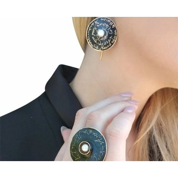 Χειρόγραφα σκουλαρίκια μακριά κρεμαστά με μαργαριτάρια - 4679, Τα χειρόγραφα σκουλαρίκια κρεμαστά με μαργαριτάρια αποτελούν μια εκλεπτυσμένη επιλογή για τη γυναίκα που αναζητά μοναδικότητα και στυλ. Σχεδιασμένα από την Ελληνίδα Σχεδιάστρια Κοσμημάτων Αικατερίνη Χαλκιαδάκη, αυτά τα εντυπωσιακά χειροποίητα κοσμήματα συνδυάζουν την κλασική ομορφιά των μαργαριταριών με τη σύγχρονη αισθητική.
Κατασκευασμένα από ποιοτικό ορείχαλκο με μαύρη πατίνα, τα σκουλαρίκια διαθέτουν κυκλικό σχήμα με χαραγμένα χειρόγραφα κείμενα που δημιουργούν έναν artistic χαρακτήρα. Το κεντρικό λευκό μαργαριτάρι σε κάθε κομμάτι προσθέτει λάμψη και κομψότητα, ενώ το χρυσαφί φινίρισμα συμπληρώνει αρμονικά τη συνολική εμφάνιση.
Αυτά τα μακριά κρεμαστά σκουλαρίκια είναι ιδανικά για εκδηλώσεις, γάμους ή καθημερινή εμφάνιση που θέλετε να ξεχωρίσει. Η χειροποίητη κατασκευή εγγυάται τη μοναδικότητα κάθε κομματιού.